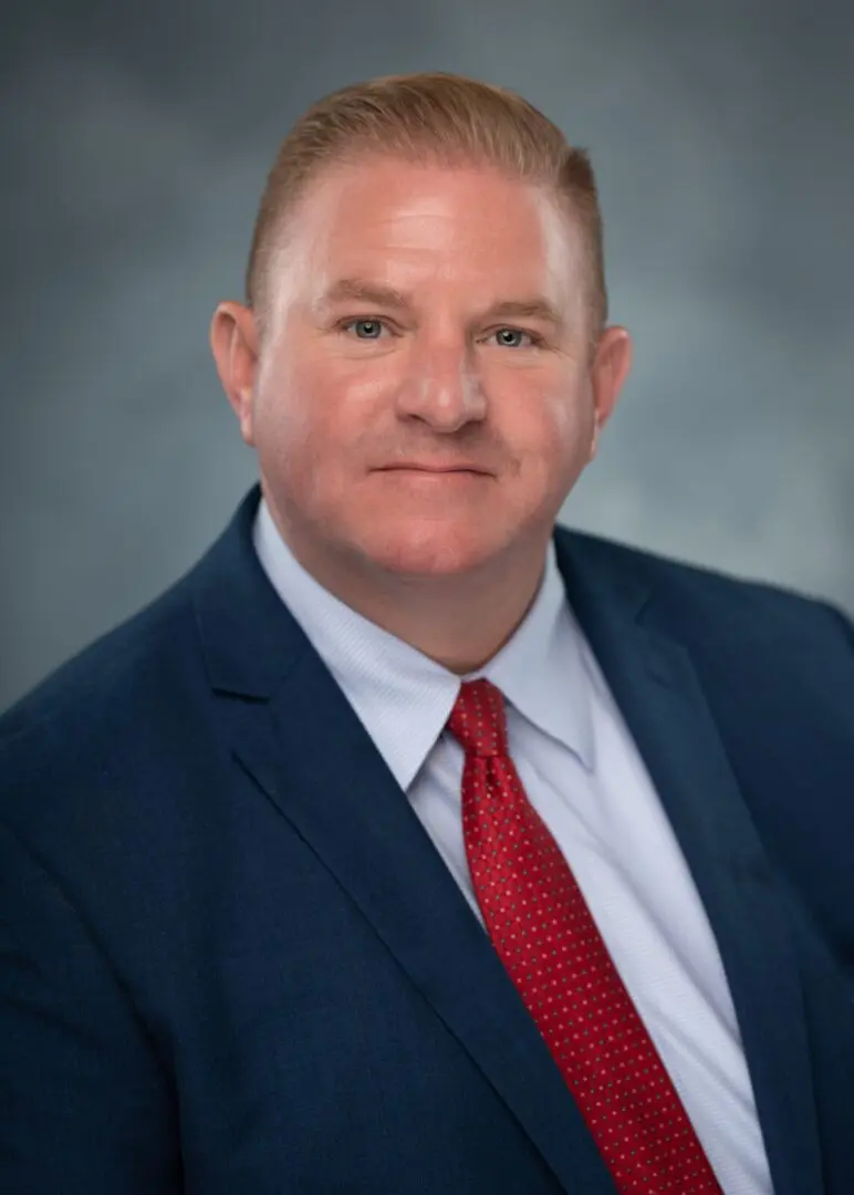 A man in a suit and tie posing for a photo representing Priority Charter Schools.